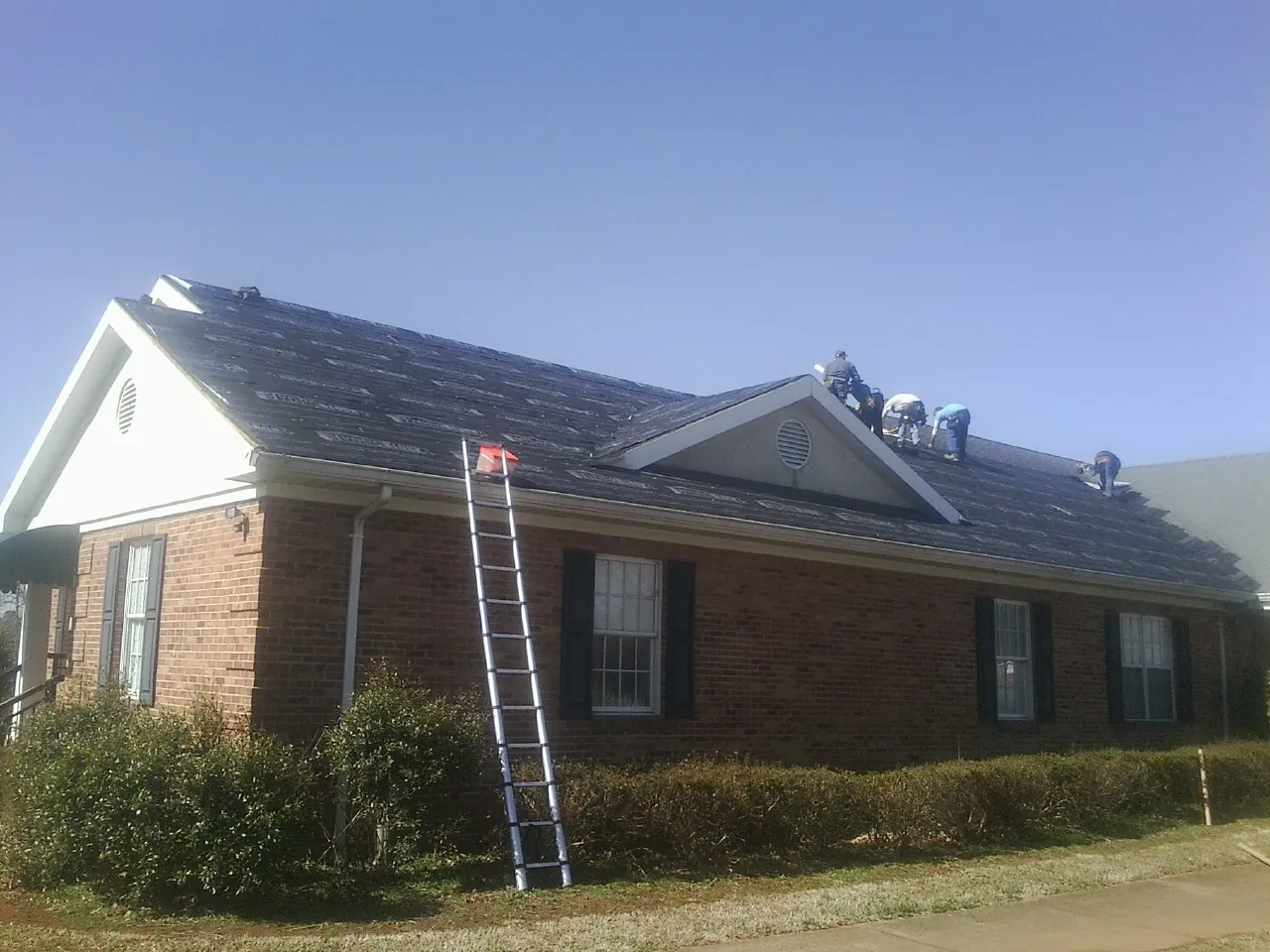 Crew tearing shingles off a brick ranch roof with a ladder set — Metal Roof Repair work by our crew in Metaline Falls