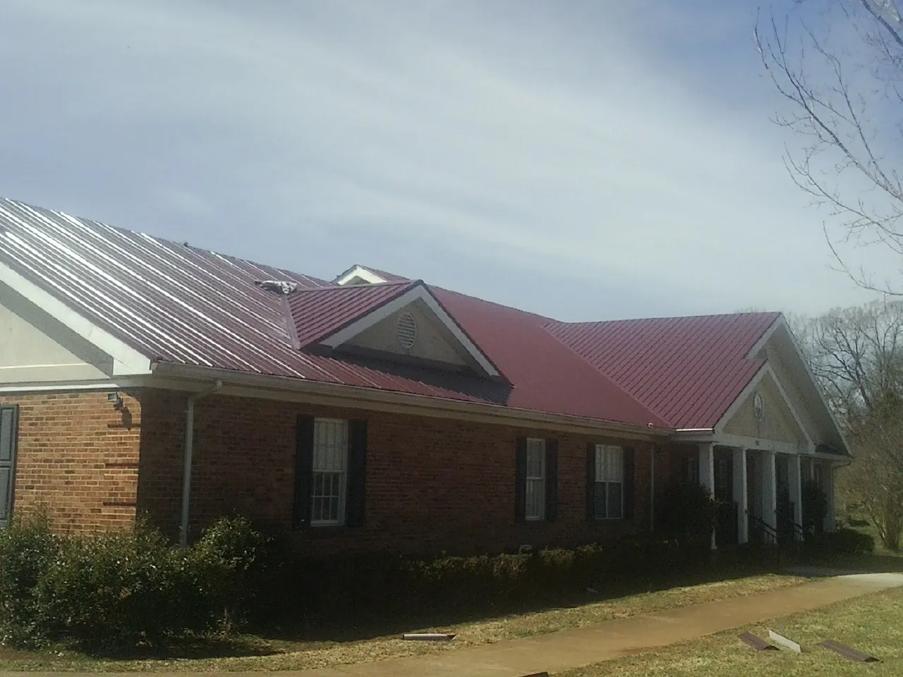 Red metal roof with gabled entries on a long brick building, from a Hail Damage Roof Repair job in Metaline Falls