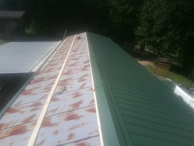 Old rusted panels beside newly installed green metal roofing — Wind Damage Roof Repair by Roofing Brothers in Metaline Falls