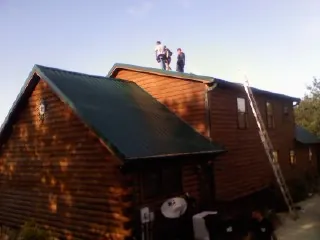Crew on the ridge of a green metal roof on a two story log home in Metaline Falls