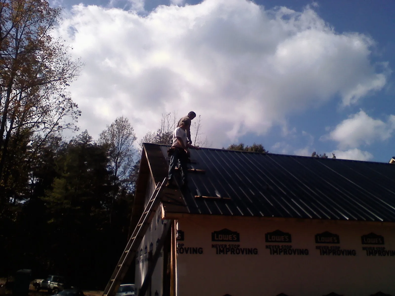Roofer fastening dark metal panels high against a cloudy sky, from a Roof Inspection job in Metaline Falls