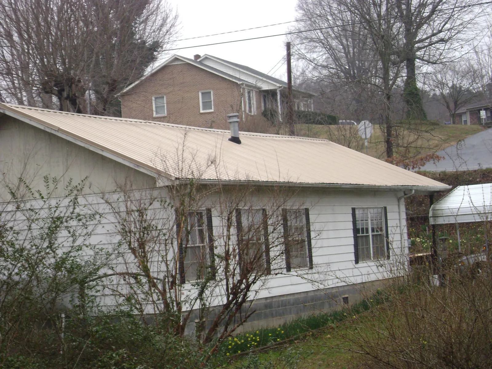 Tan metal roof on a white sided house set into a hillside — Commercial Roofing by Roofing Brothers in Metaline Falls
